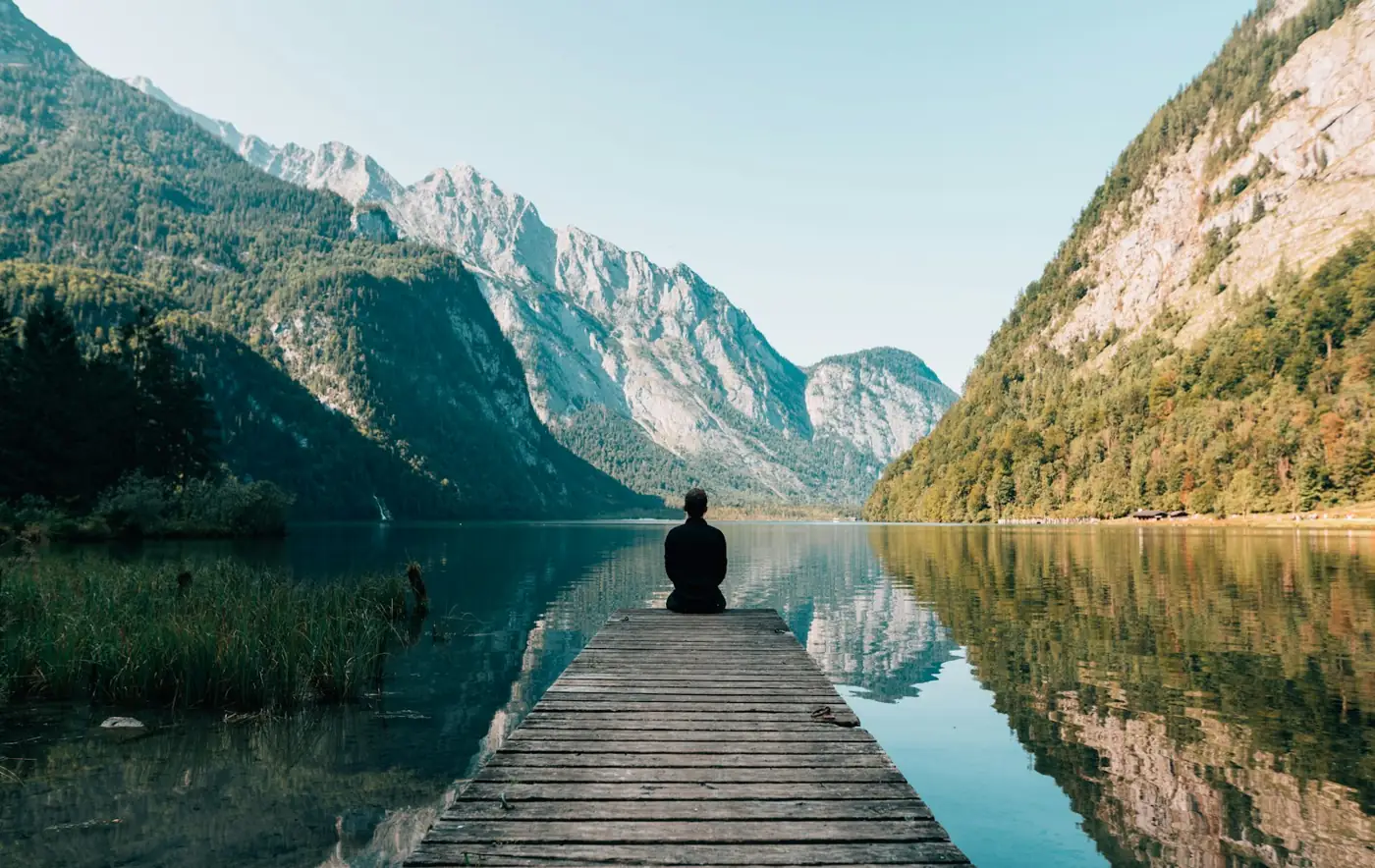 A person sitting alone at the end of a jetty on a still lake