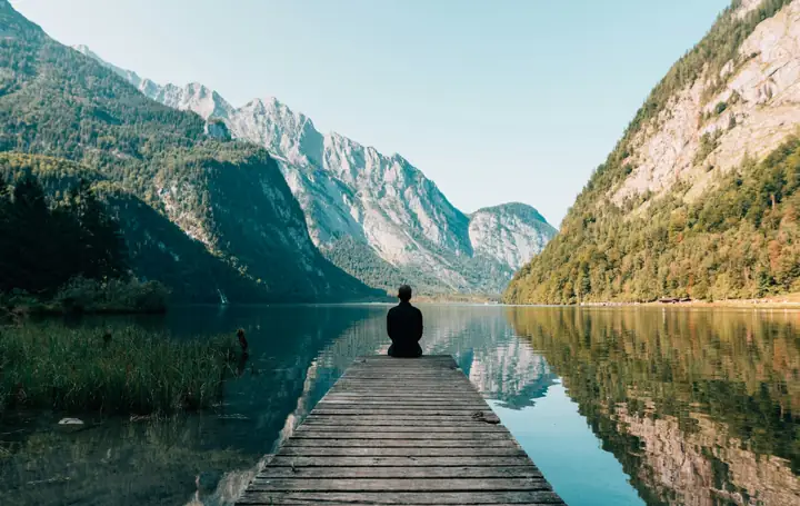 A person sitting alone at the end of a jetty on a still lake